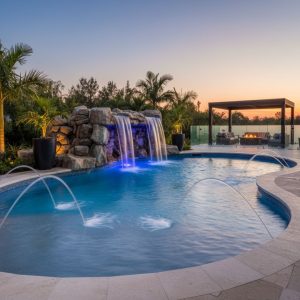 A close-up of a custom pool's edge with three elegant, arched sheer-descent fountains creating a tranquil, flowing wall of water into the pool.