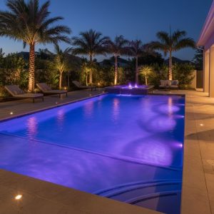A modern inground pool at night, illuminated by vibrant blue and purple energy-efficient LED underwater lighting, creating a dramatic and elegant ambiance.